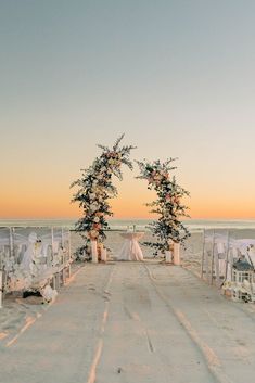 an outdoor ceremony set up on the beach with white linens and floral arch decorations