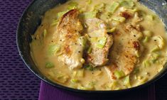 a pan filled with chicken and noodles on top of a purple place mat next to a spoon