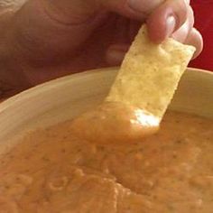 a hand holding a tortilla chip over a bowl of ranch dip refried beans, shredded cheddar cheese, ranch dressing mix, and sour cream