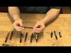 a man is holding an electronic device in front of many pens on a table top