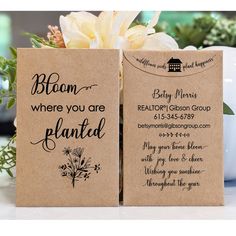 two brown paper bags with black writing on them sitting next to flowers and a white vase