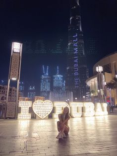 a woman kneeling down in front of a sign that says i love you at night