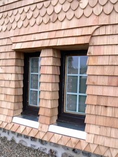 two windows with wooden shingles on the side of a house