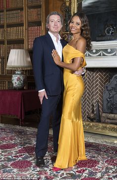 a man and woman standing next to each other in front of a fire place with bookshelves