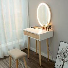 a white vanity table with a lighted mirror and stool in front of it next to a window