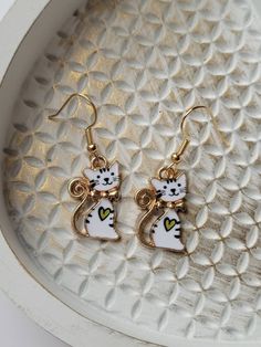 These cute, white cat earrings are so sweet! The little kitty even has a heart on its chest, making it even more endearing! The drop length is about 1.5 inches and the width is about .5 inches. They are made of zinc alloy and enamel. These whimsical earrings are lightweight making them comfortable to wear and ideal for older kids, teens, and adults. The ear wires are gold in color, hypoallergenic, and nickel-free. Each pair comes with two, clear rubber backs. They would make a perfect gift for a Cute Cat Ears Earrings With Cat Print, Cute Cat Print Jewelry Gift, White Metal Heart Earrings For Gift, White Metal Heart Earrings Gift, Cute Metal Jewelry With Cat Design, Cute Cat Design Dangle Earrings, Cute Hypoallergenic Cat Ears Jewelry, Cute Cat Design Drop Earrings, Cat Design Earrings With Cat Ears For Gifts