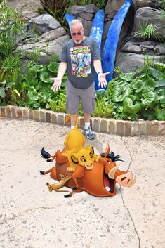 a man standing in front of a fake lion laying on the ground next to another animal