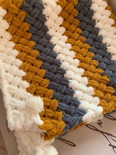 a crocheted blanket is laying on top of a bed with white and yellow colors