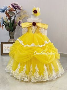 a yellow dress with white lace and flowers on the top is displayed in front of a vase