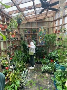 a woman standing in a greenhouse filled with lots of plants