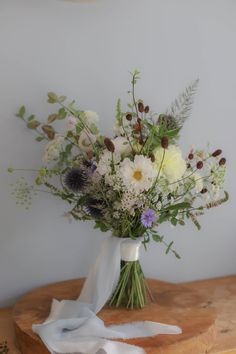 a vase filled with white and purple flowers on top of a wooden table next to a wall