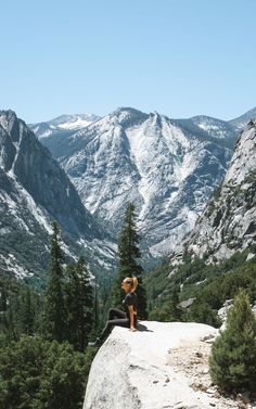 a person sitting on top of a rock with mountains in the background