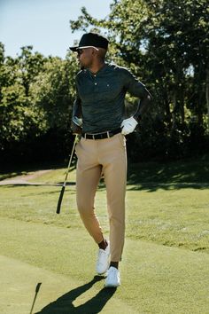 a man walking across a grass covered golf course with a club in his hand and hat on