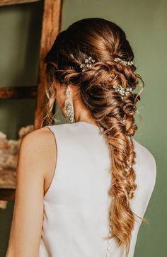 a woman with long hair wearing a white dress and pearls in her hair, looking back at the camera