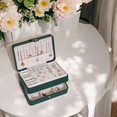 an open jewelry box sitting on top of a white table next to pink and yellow flowers