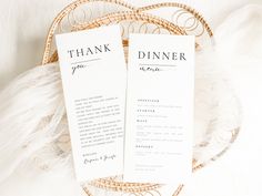 two wedding program cards sitting on top of a wicker basket with feathers around it