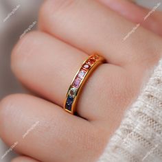 a woman's hand wearing a gold ring with multicolored stones