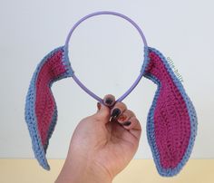 a hand holding a purple and blue crocheted headband with two ears on it