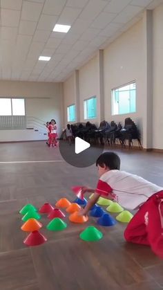 two children playing with plastic cups on the floor in an empty room, while another child watches