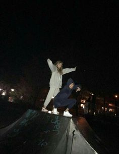 two young people are skateboarding on the edge of a half pipe at night time