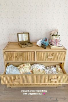 a wicker dresser with two drawers and a mirror on the top, in front of a floral wallpapered wall