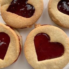 four heart shaped cookies sitting on top of a white plate with jam in the middle