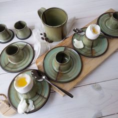 an assortment of tea cups and saucers on a wooden tray with eggs in them