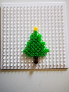 a green lego christmas tree sitting on top of a white board with yellow and orange decorations