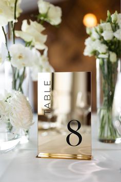 the table numbers are displayed in glass vases with white flowers behind them, along with other decorations