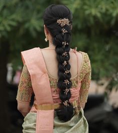 a woman with long black hair wearing a pink and green saree, braided into a ponytail