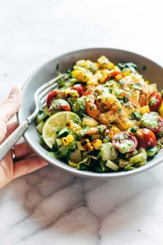 a hand holding a bowl filled with salad and shrimp on top of a marble counter