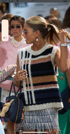 a woman is walking down the street with her hand on her hip and wearing a multicolored sweater