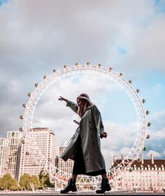 a woman is standing in front of a ferris wheel with her hand out to the side