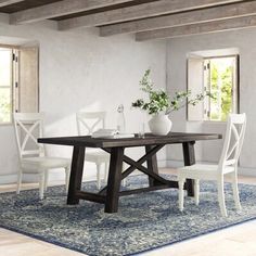 a dining room table with white chairs and a blue area rug in front of it