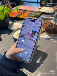 a person holding an iphone in front of a table full of plates and bowls of food