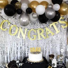 a table topped with a cake covered in white frosting and black and gold balloons