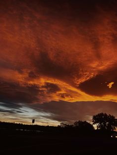 the sky is red and orange as the sun sets in the distance with trees on either side