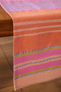 an orange and pink striped table cloth on a wooden table with two chairs in the background