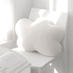 a white cloud shaped pillow sitting on top of a chair next to an open book