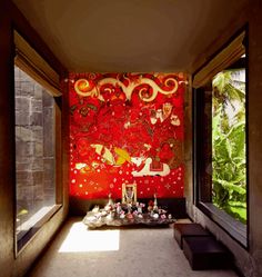 a red wall in the middle of a room with two windows on each side and an artistic painting on the wall behind it