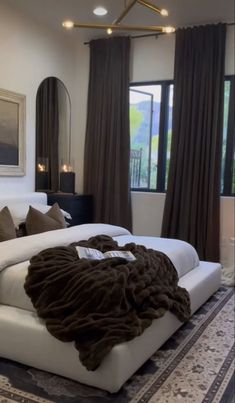 a large white bed sitting inside of a bedroom next to a tall window filled with curtains