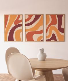 three abstract paintings hang on the wall above a round table with two chairs and a vase