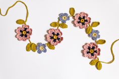 two crocheted flowers on a white surface with yellow and blue yarn around them