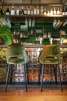 two green velvet chairs sitting in front of a bar