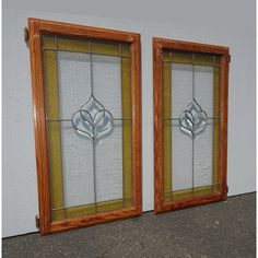 two stained glass windows sitting next to each other on a cement floor in front of a white wall