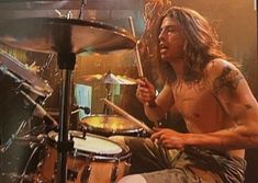 a man with long hair playing drums in front of a tv screen showing him drumming