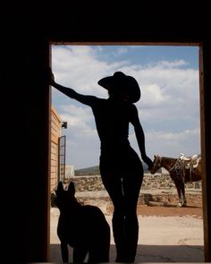 a woman standing next to a dog in front of a horse and cow silhouetted against a blue sky