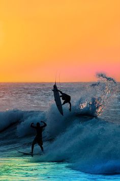 two surfers are riding the waves in front of an orange sky at sunset or sunrise