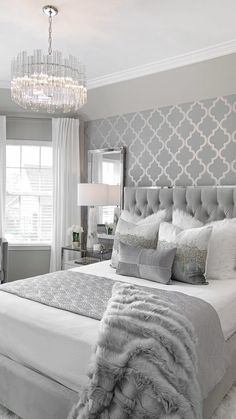 a bedroom with a bed, chandelier and two chairs in front of the window