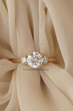 an engagement ring with three diamonds on it sitting on top of a beige fabric background